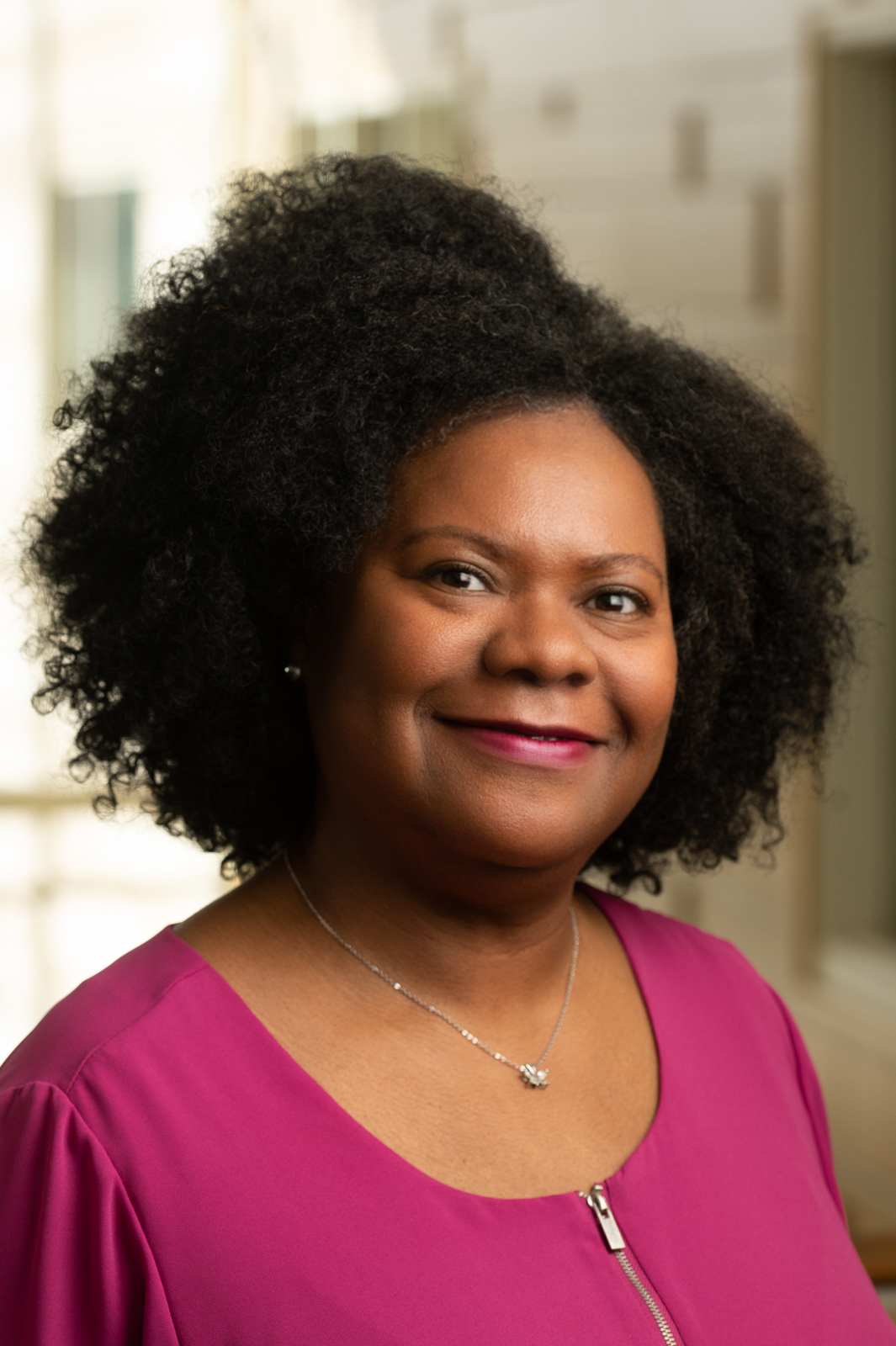 A smiling woman with parted curly hair, wearing a necklace