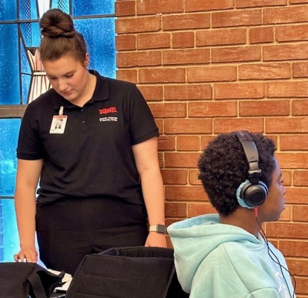 One grad student checking equipment while monitoring client in chair with headphones on