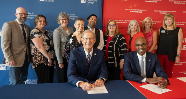 Group photo with two sitting and the rest standing in the background at signing ceremony