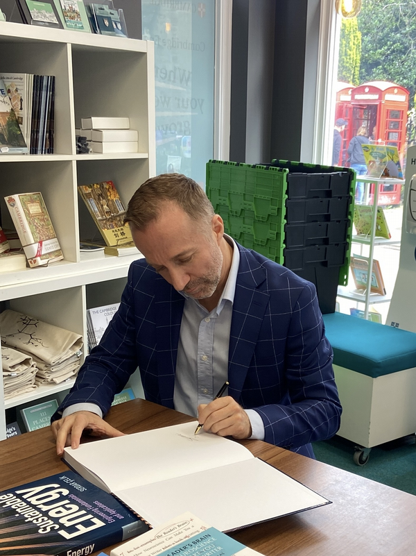 Celik at a table in a bookstore signing his book