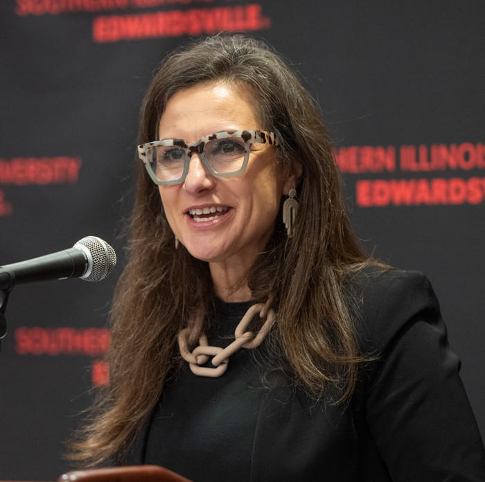 Elza Ibroscheva wearing large framed glasses and a chain necklace speaking into a microphone