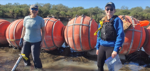 Two women standing in a river next to large orange buoys