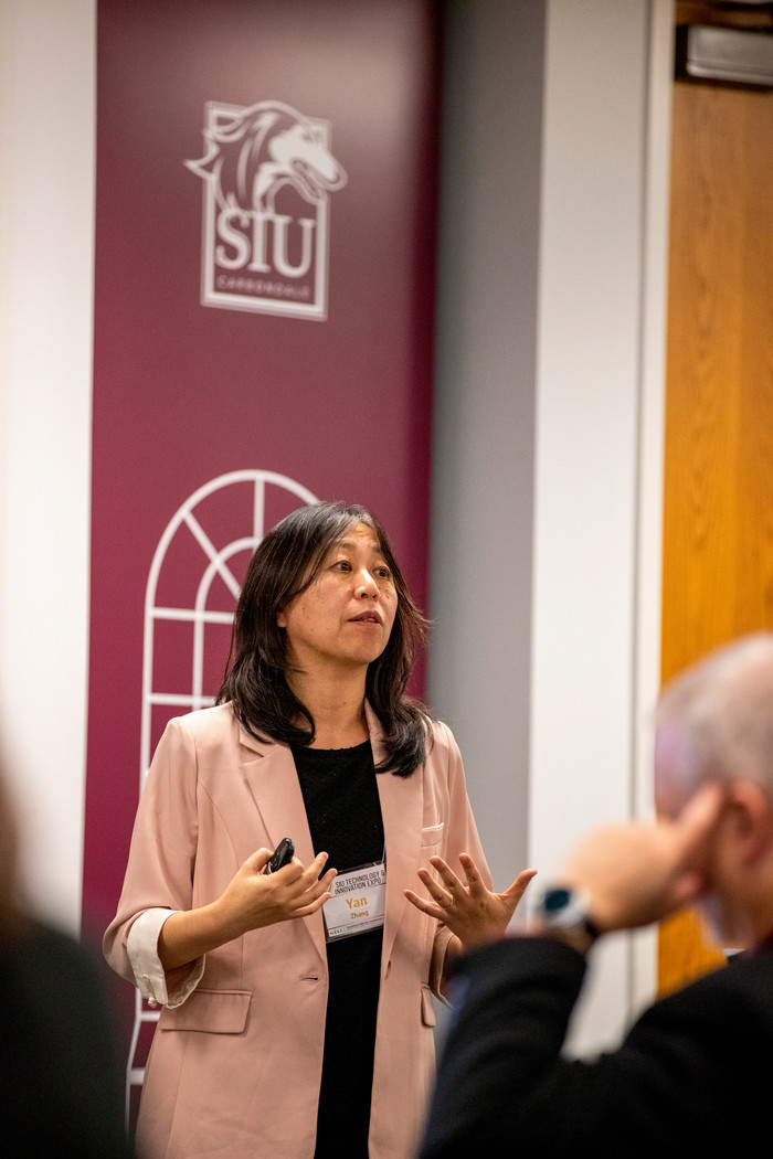 photo of Yan presenting with arms open in front of a podium