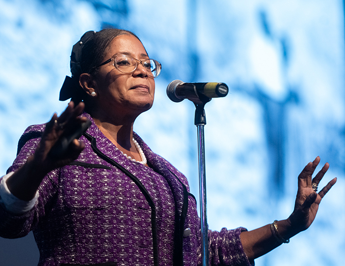 Abernathy speaking in the SIUE Meridian Ballroom in front of a photo of Dr. King, gesturing with her hands open and a pensive face